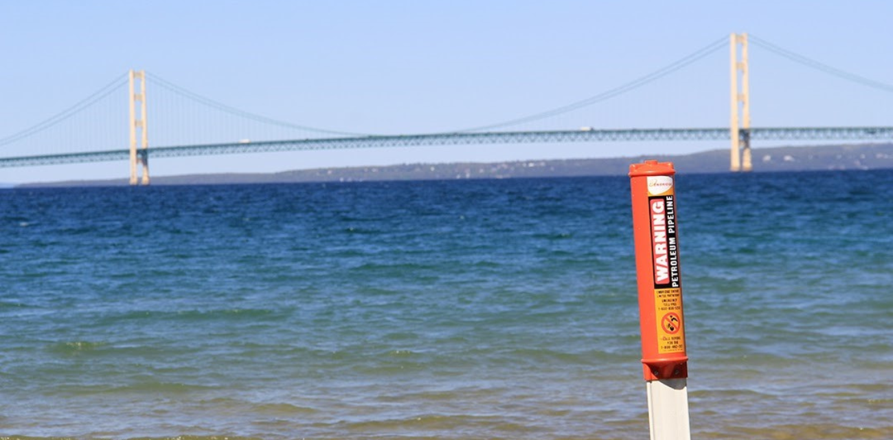 A warning marker sits at the water's edge with the Mackinac Bridge in the background