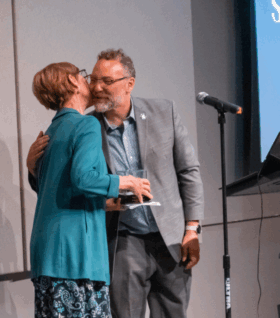 Sandra Sorini Elser hugs Conan Smith after receiving the 2024 Petoskey Prize for Environmental Leadership