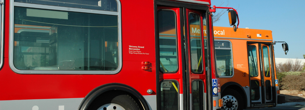 A red bus sits parked next to an orange bus