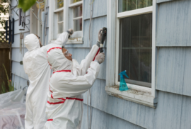 Workers clad in white suits remove lead from the exterior paint of a home. (Photo via Adobe)