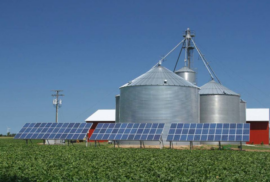 Solar panels gather sunlight in front of silos on a farm