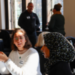 Two women discuss pressing environmental issues at the 2023 MEC Annual Meeting; two additional participants stand just out of focus in the background.