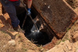 A man breaks apart a water outlet in an old septic tank. (Photo via Adobe)