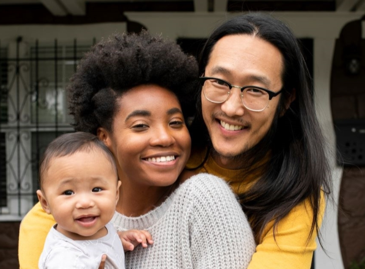 A multicultural family smiles for the camera on their front porch.