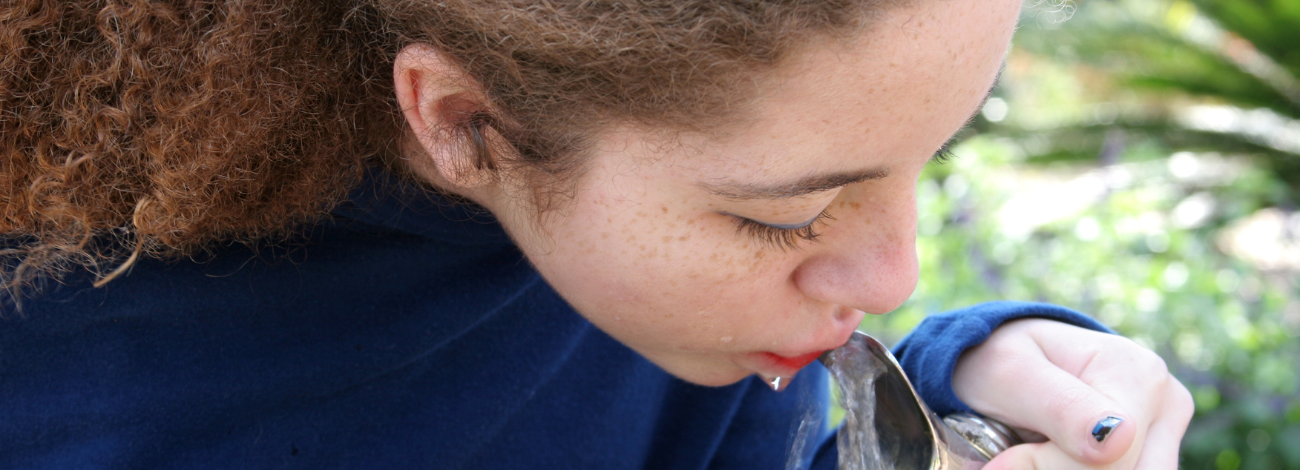 A young girl with brown curly hair leans over to get a drink from a public drinking fountain