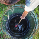 A technician reaches down to clear debris in a septic tank