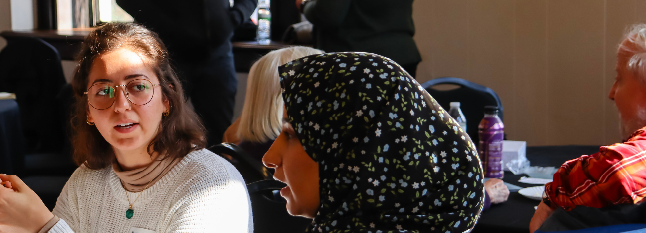 Two women discuss pressing environmental issues at the 2023 MEC Annual Meeting; two additional participants stand just out of focus in the background.