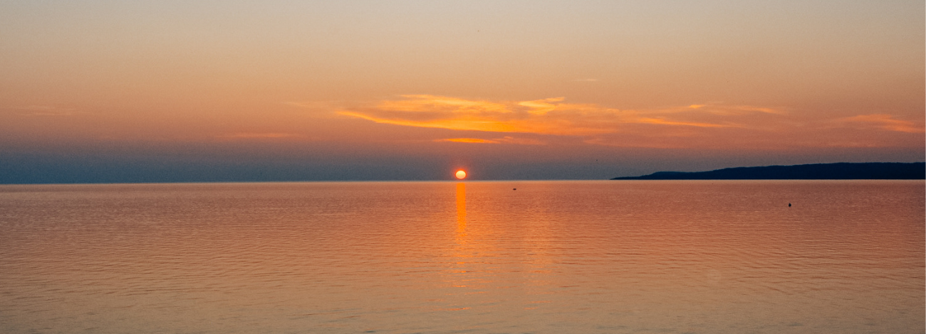 The sun sets in Petoskey on a beautiful summer evening, hues of orange, purple and yellow on the water and in the sky.