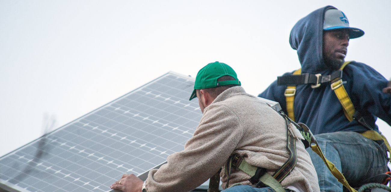 Workers install a solar panel on top of the Michigan Environmental Council's Lansing office roof