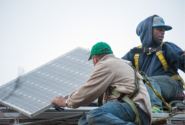 Workers install a solar panel on top of the Michigan Environmental Council's Lansing office roof