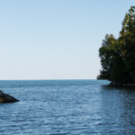 Lake Huron's waters are peaceful and serene on a bright summer day, pictured alongside a tree-dense shoreline