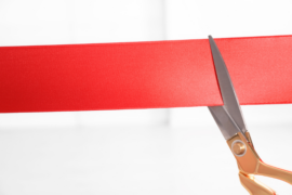 A large red ribbon sits on a white background as scissors prepare to cut the ribbon.