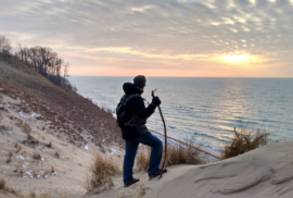 A hiker pauses atop a dune to look at the sky