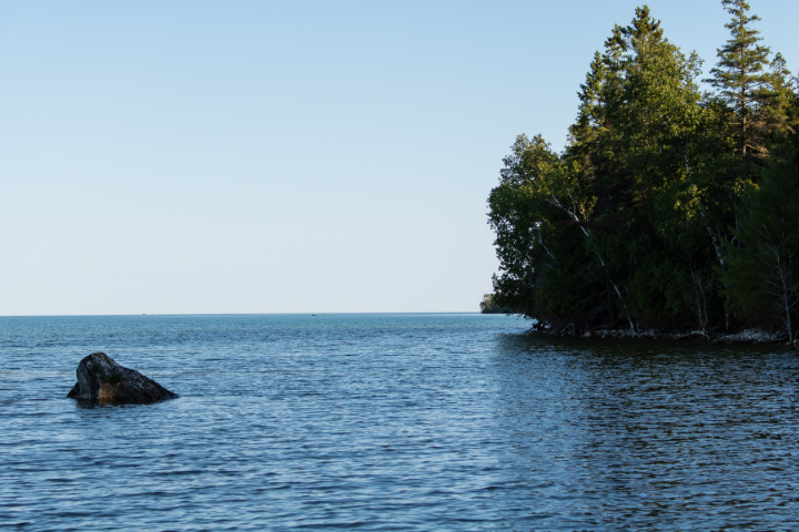 A large rock sits serenely near the Lake Huron shoreline. A few trees dot the shore on the right