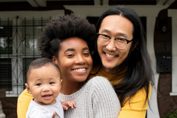 A multicultural family smiles for the camera on their front porch steps. 