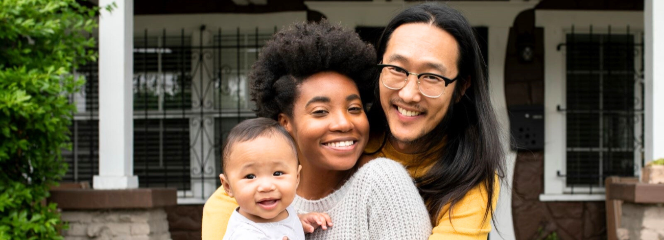 A multicultural family smiles for the camera on their front porch steps.