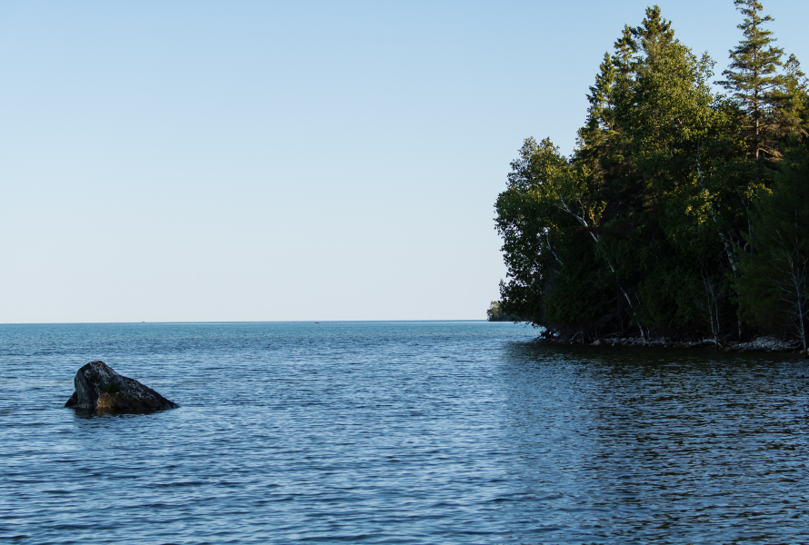 A large rock sits serenely near the Lake Huron shoreline. A few trees dot the shore on the right