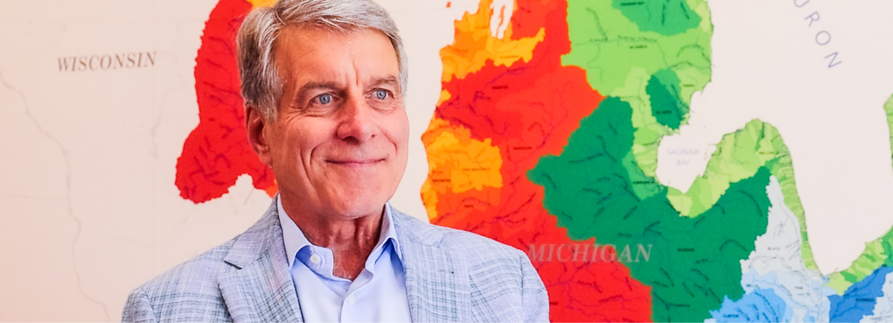 A photo of John Erb, chairman for the Erb Family foundation, seated in front of a large map of Michigan's watersheds.