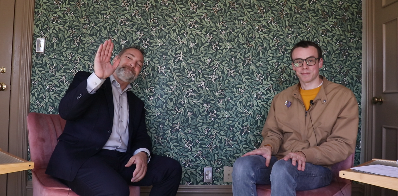 Conan Smith waves at the camera while Beau Brockett looks on while filming a podcast episode on recycling.