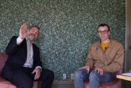 Conan Smith waves at the camera while Beau Brockett looks on while filming a podcast episode on recycling.