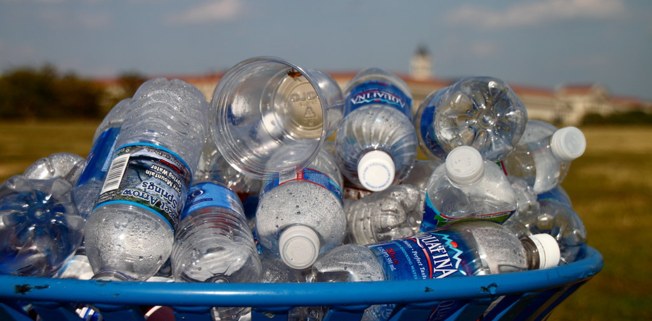 Plastic water bottles nearly overflow a blue trash can.