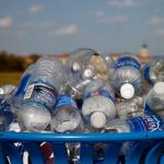 Plastic water bottles nearly overflow a blue trash can.