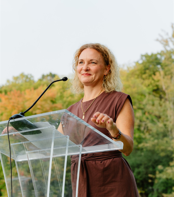 Rebecca Esselman smiles while at a podium against a backdrop of trees. (Photo courtesy of Rebecca Esselman)