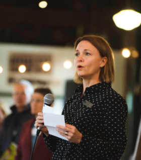 Rebecca Esselman speaks through a microphone to an audience at an event