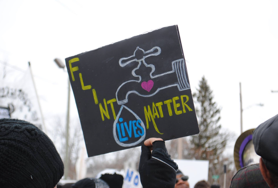 A handmade sign reading "Flint Lives Matter" and featuring a dripping water faucet is held outdoors. (Photo courtesy of Flint Rising.)
