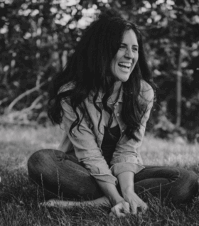 Jaime Churches laughs while sitting cross-legged in the grass