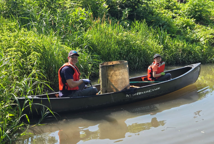 A man and child in a canoe pose for a photo while picking up trash along the Detroit River. (Photo courtesy of Friends of the Detroit River.)