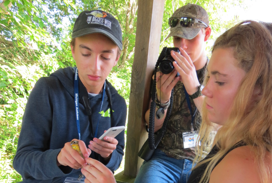 Participants of the A member of the Michigan Young Birders Camp holds a bird while two other teens interact with it. (Photo courtesy of Michigan Audubon)